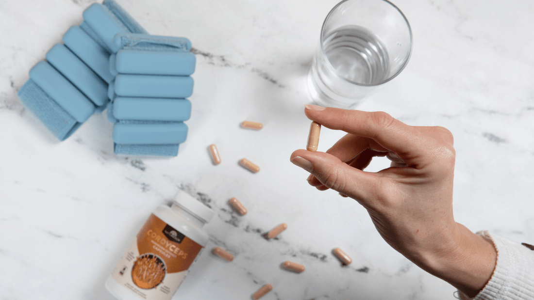 Naturealm Cordyceps Capsules in Hand with Marble Counter Background Glass of Water Blue Wrist Weights