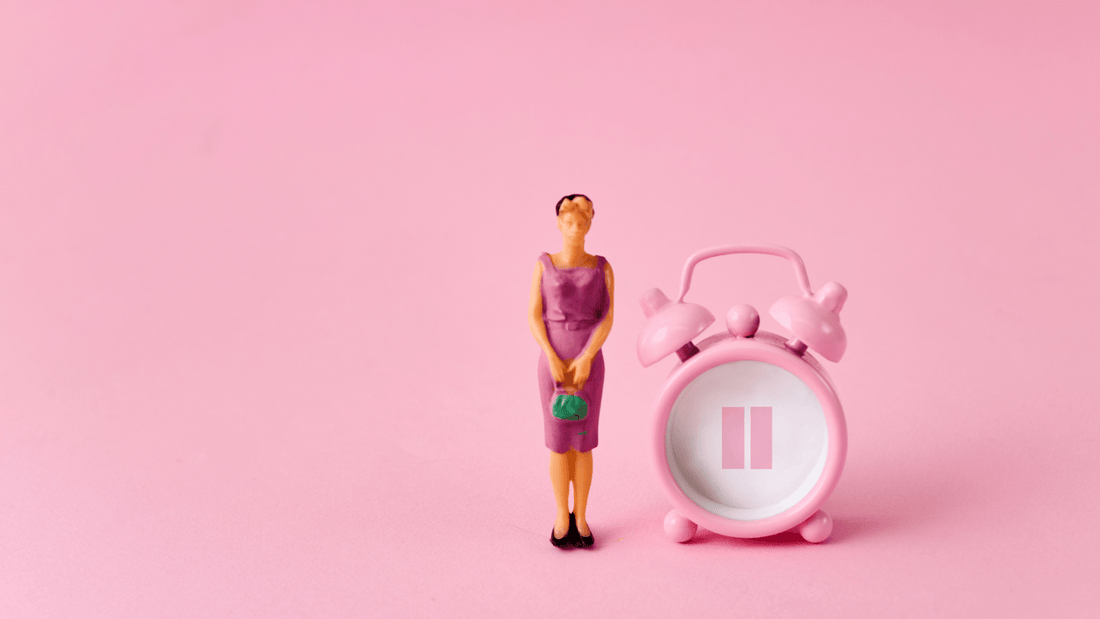 Orange figurine of a woman on a pink background with a pink alarm clock with the pause symbol on it