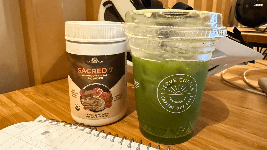 Sacred 7 Mushroom Extract Powder 2.1 oz jar next to iced matcha tonic with bike helmet in background and notebook in foreground