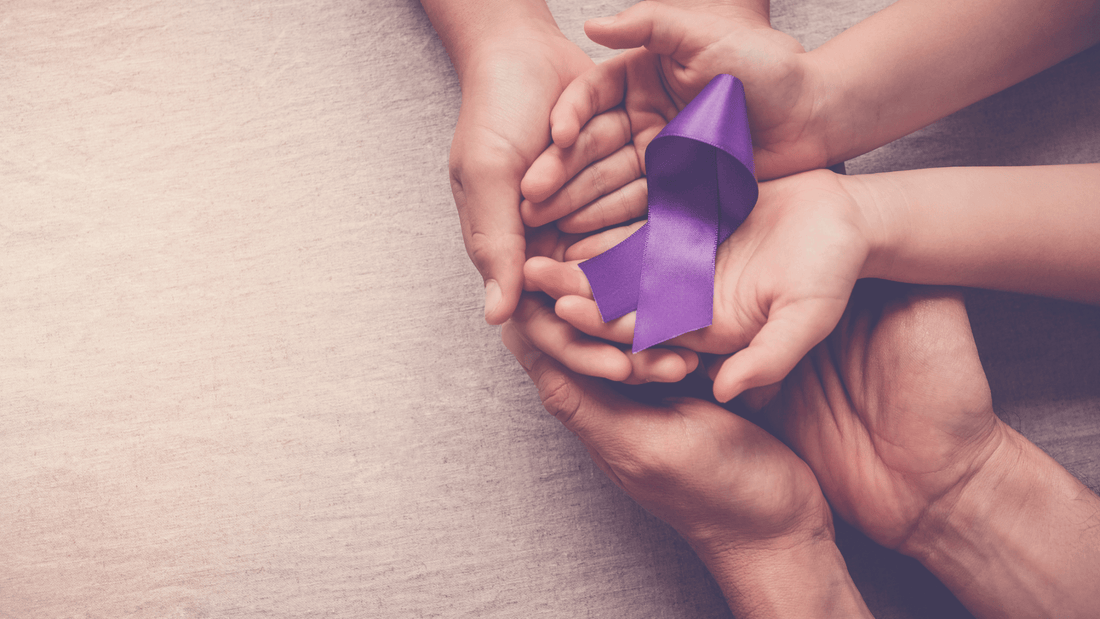 Two adult hands holding two child hands with purple folded ribbon for epilepsy awareness in child's hands on a tan fabric background